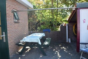 A patio area with a picnic table and benches, a metal pole, and a brick wall. - Holiday apartment with 2 bedrooms (Petten)