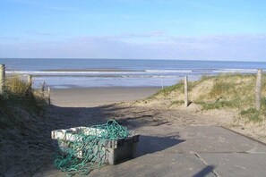 A beach with a concrete path leading to the water, a pile of green nets, and a wooden fence. - Holiday apartment with 2 bedrooms (Petten)