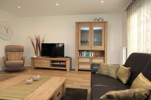 Ein Wohnzimmer mit Ledersofa, Relaxsessel, Holzschrank mit Glastüren, Fernseher und Couchtisch.
