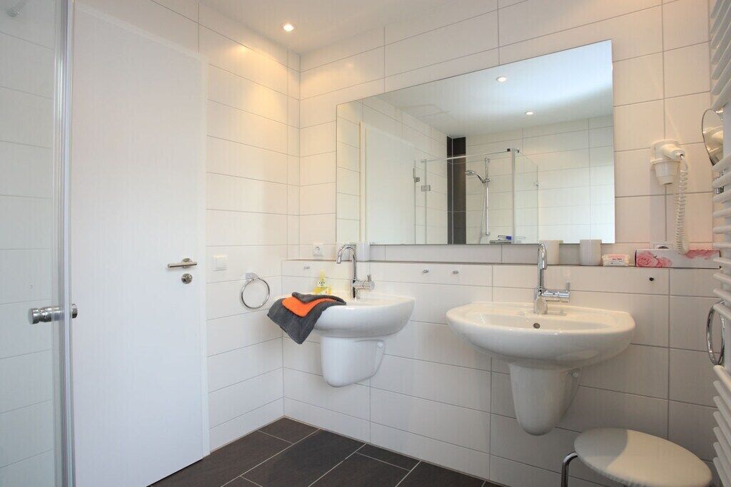 Ein modernes Badezimmer mit Toilette, zwei Waschbecken, einer Dusche und einem Spiegel.