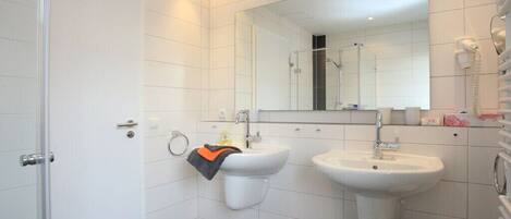 Ein modernes Badezimmer mit Toilette, zwei Waschbecken, einer Dusche und einem Spiegel.