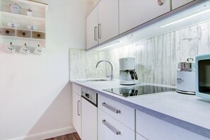A modern kitchen with white cabinetry, a stainless steel sink, and a coffee maker. - Villa by the sea, home port (Sankt Peter-Ording)