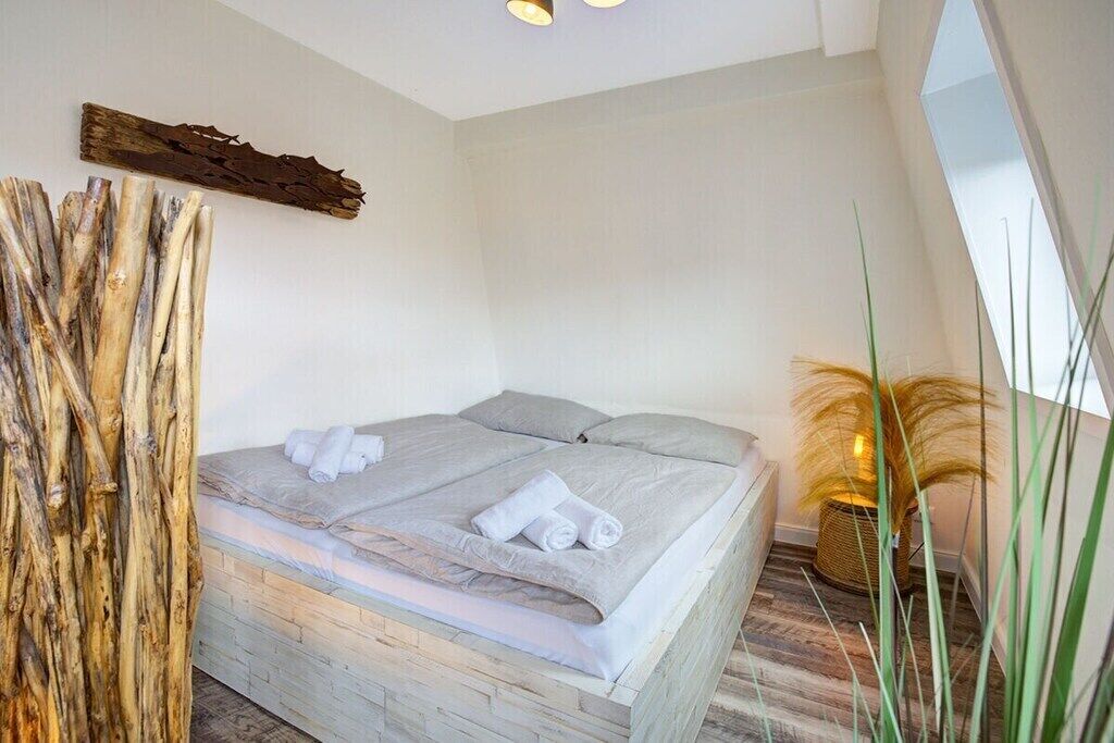 A bedroom with a bed, towels, a wooden wall decor, and a plant.