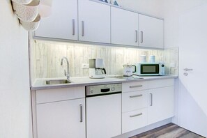 A compact kitchen with white cabinets, a Bosch dishwasher, a microwave, and a coffee maker. - Villa by the sea, home port (Sankt Peter-Ording)