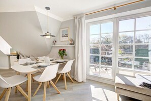 A dining area with a table set for four, a hanging light fixture, and a view of the outdoors through large windows. - Holiday apartment with 2 bedrooms (Sankt Peter-Ording)