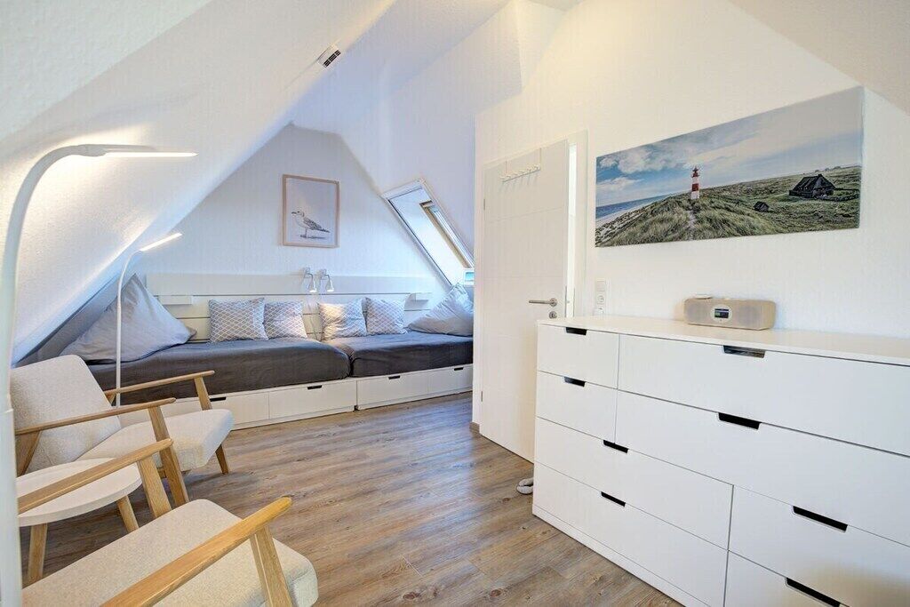 A compact room with a loft bed, built-in storage, and a painting of a coastal scene.