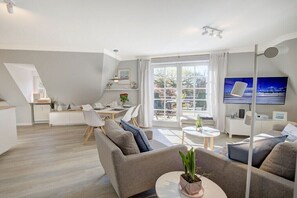A modern living room with a sofa, TV, and dining area. - Holiday apartment with 2 bedrooms (Sankt Peter-Ording)