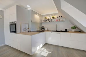 A modern kitchen with white cabinetry, a built-in oven, a sink, and a countertop with various items. - Holiday apartment with 2 bedrooms (Sankt Peter-Ording)