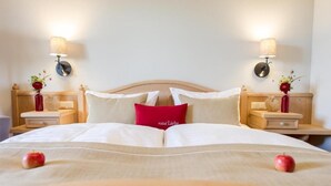 A neatly made bed with a red pillow, two bedside tables with lamps, and a vase with flowers on each side. - Hotel Sankt Leonhard (Bad Birnbach)