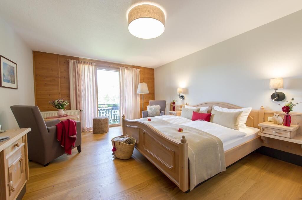 A hotel room with a large bed, a desk, a chair, a small table, and a window with curtains.