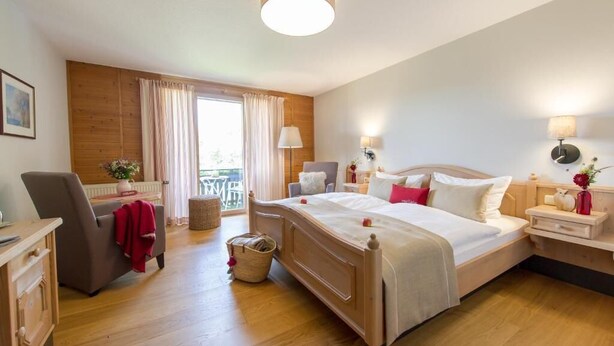 A hotel room with a large bed, a desk, a chair, a small table, and a window with curtains. - Hotel Sankt Leonhard (Bad Birnbach)