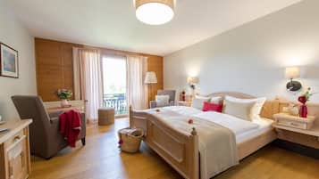 A hotel room with a large bed, a desk, a chair, a small table, and a window with curtains.