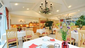 A hotel dining area with tables set for service, a reception desk, and a view of the kitchen. - Hotel Sankt Leonhard (Bad Birnbach)
