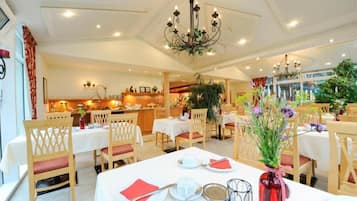 A hotel dining area with tables set for service, a reception desk, and a view of the kitchen.