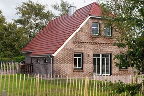 A brick house with a red roof, a garage, and a wooden fence. - Holiday home in the North Sea with 3 bedrooms (Nessmersiel)