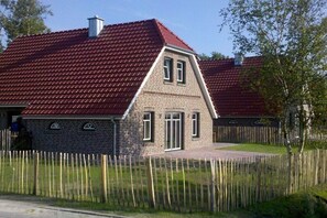 Una casa de dos pisos amb teules vermelles i una tanca de fusta.