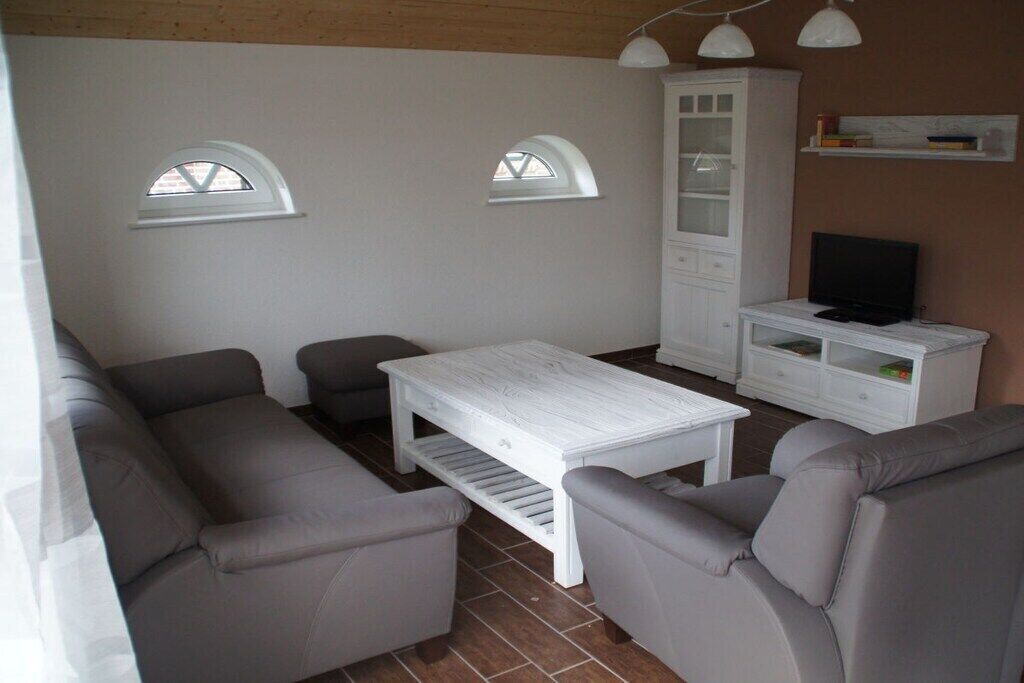 A living room with a sofa set, a white coffee table, a cabinet, a television, and two arched windows.