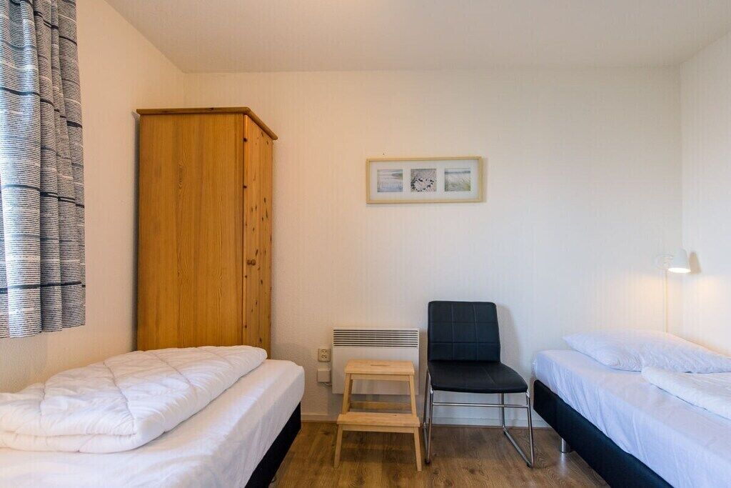 Une petite chambre propre, avec deux lits simples, une armoire en bois, un radiateur et un tableau encadré au mur.