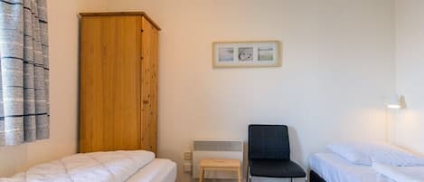 Une petite chambre propre, avec deux lits simples, une armoire en bois, un radiateur et un tableau encadré au mur.