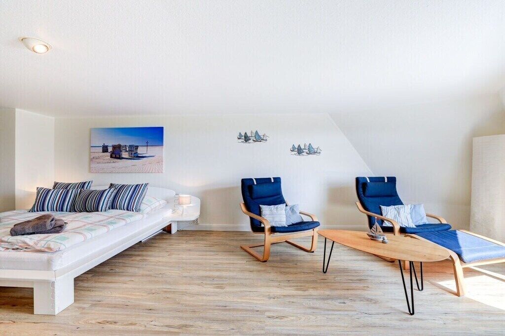A modern bedroom with a bed, two blue chairs, a small table, and a painting on the wall.