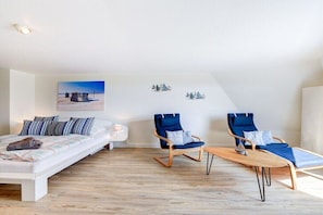 A modern bedroom with a bed, two blue chairs, a small table, and a painting on the wall. - Holiday home with 1 bedroom (St. Peter-Ording)