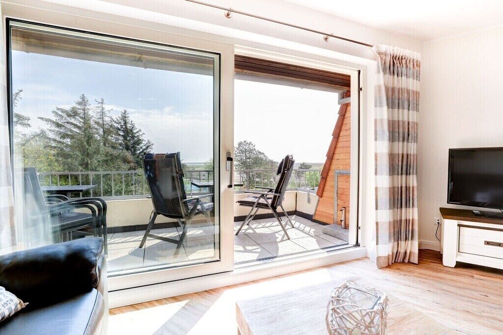 A modern living room with a sofa, a TV, and a balcony with chairs.