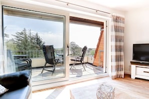 A modern living room with a sofa, a TV, and a balcony with chairs. - Holiday home with 1 bedroom (St. Peter-Ording)