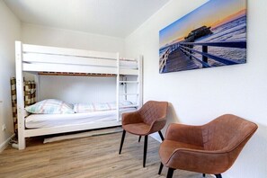 A bunk bed with a lower bunk, a pair of brown chairs, and a painting of a pier on the wall. - Holiday home with 1 bedroom (St. Peter-Ording)