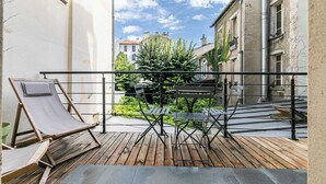 Ein Balkon mit Holzboden, Metallgeländern und Blick auf eine enge Straße mit Gebäuden und Grünflächen.