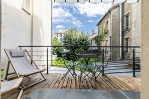 Un balcon dot é d’un plancher en bois, de rampes en métal et offrant une vue sur une rue étroite bordée d’immeubles et de verdure.