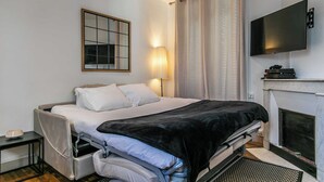 Ein modernes Schlafzimmer mit Bett, Nachttisch, Lampe, Fernseher und Kamin.