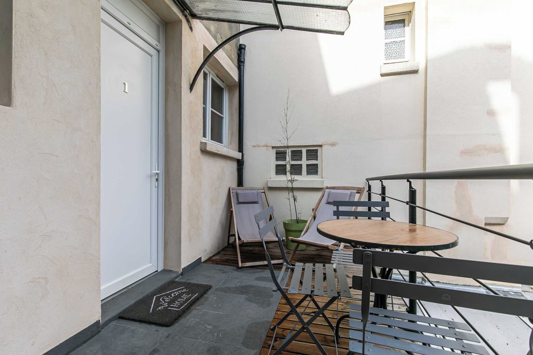 A small outdoor patio with a table and chairs, a doormat, a window, and a door.