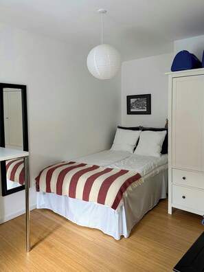 Un dormitorio con cama, mesita de noche, armario, lámpara colgante y un cuadro en la pared.