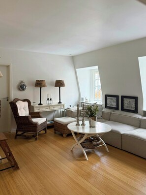 A living room with a round table, a sofa, a wicker chair, a lamp, and a clock on the wall. - Rooftop flat near Gammel Strand and Tivoli (København K)