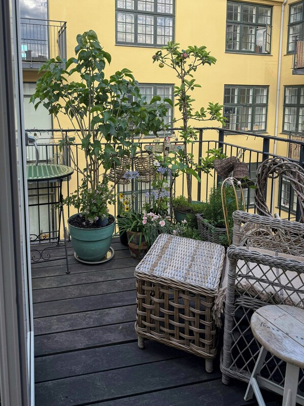 A balcony with wicker furniture, potted plants, and a view of a yellow building. - Rooftop flat near Gammel Strand and Tivoli (København K)