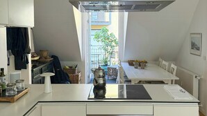 Moderni keittiö, jossa on valkoiset kaapit, sisäänrakennettu uuni ja ruostumattomasta teräksestä valmistettu liesituuletin.