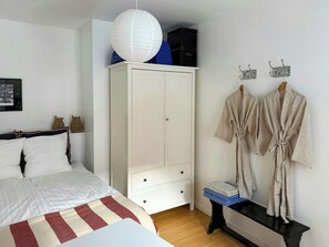 A bedroom with a bed, a wardrobe, a bench, and a hanging robe rack. - Rooftop flat near Gammel Strand and Tivoli (København K)