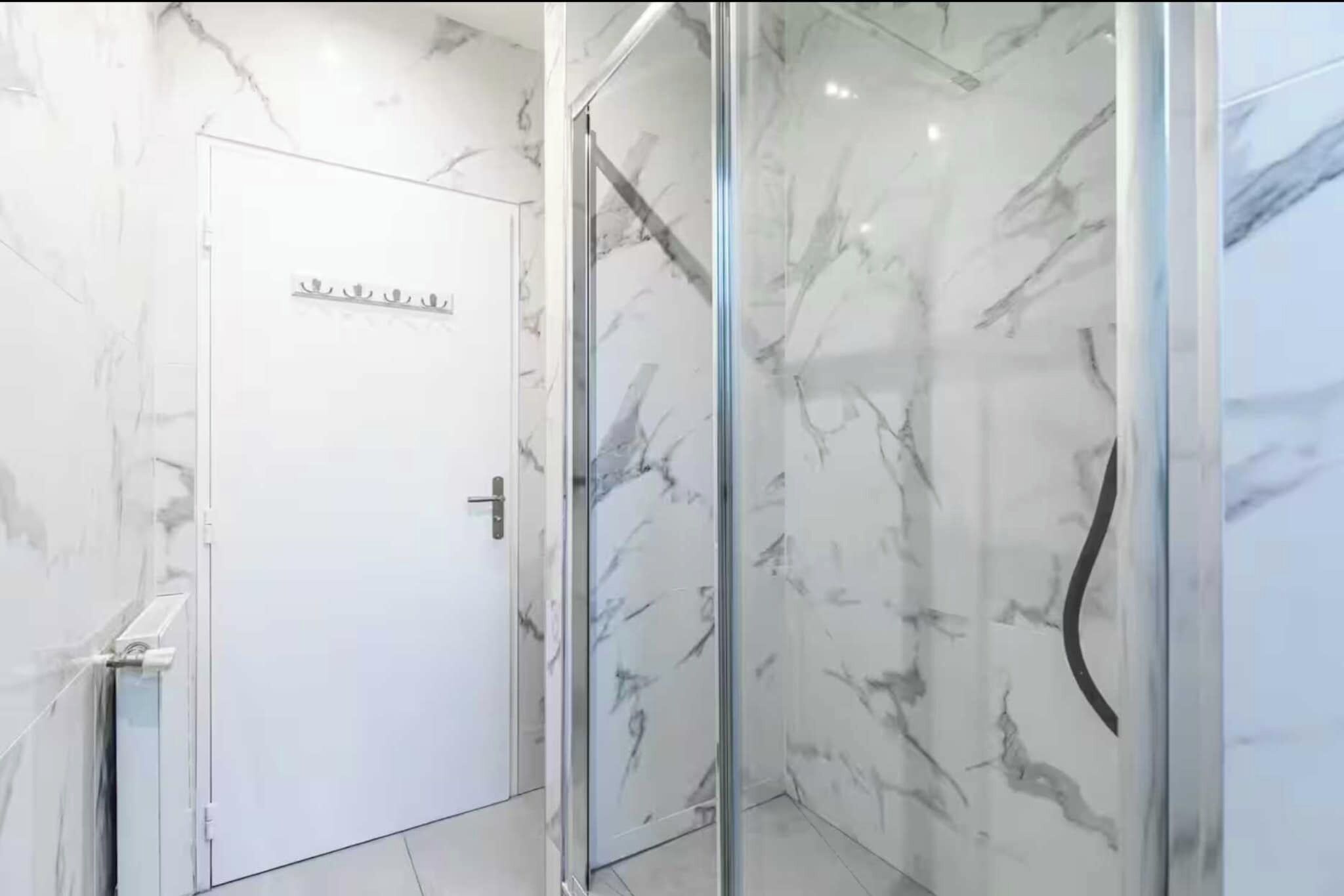 A modern bathroom with a glass shower enclosure and a white door with a towel rack.