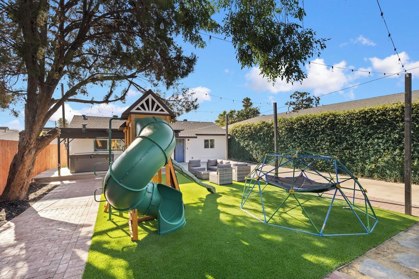 A playground with a slide and swings, surrounded by a lawn and a house.