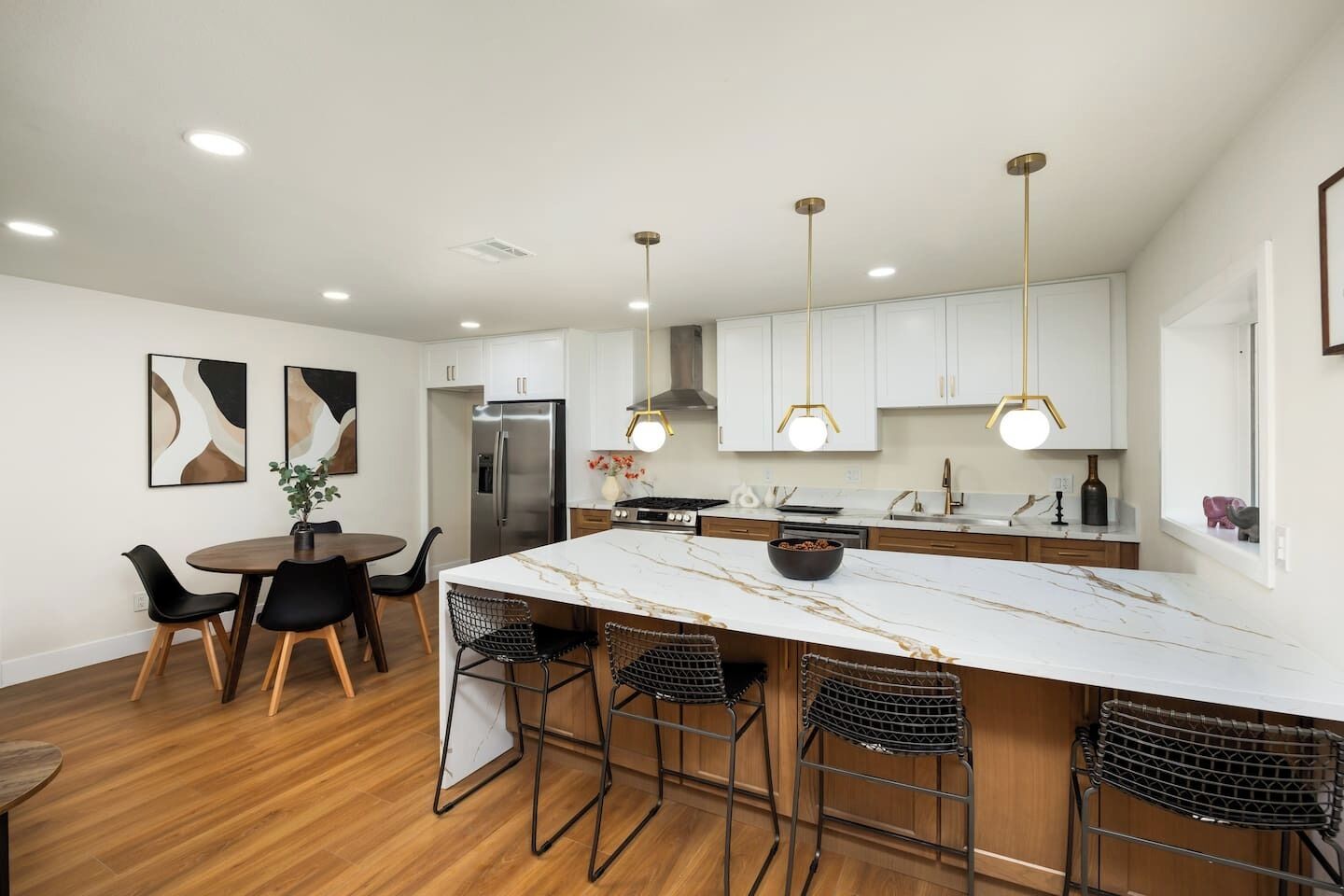 A modern kitchen with a marble island, black bar stools, and pendant lighting.