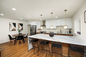 Una cocina moderna con una isla de mármol, taburetes negros y luces colgantes.