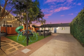 Un cortile residenziale con un'area giochi, una zona relax coperta e una casa.