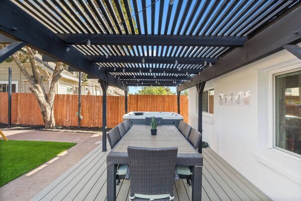 An outdoor patio with a pergola, a hot tub, and a dining table with chairs.