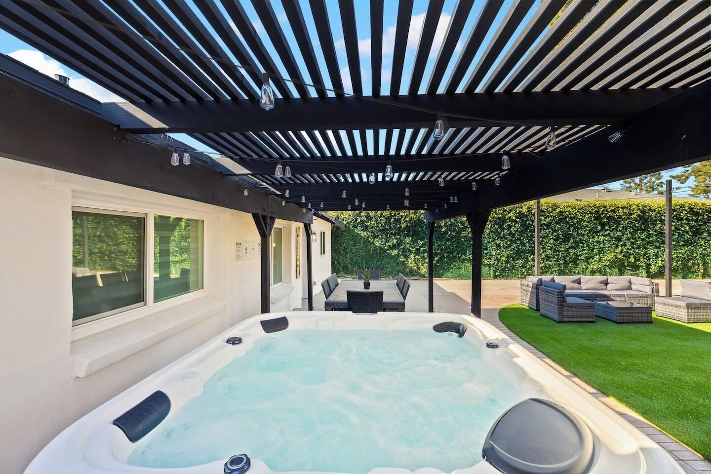 Ein Whirlpool unter einer Pergola mit einem Rasen und Gartenmöbeln.