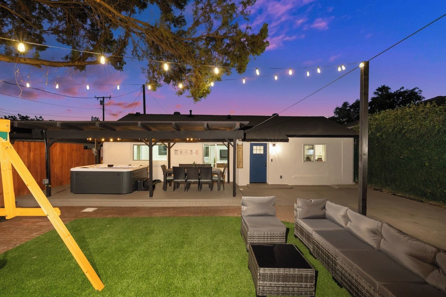 A backyard with a hot tub, outdoor seating, and a covered patio area.