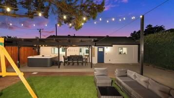 A backyard with a hot tub, outdoor seating, and a covered patio area.