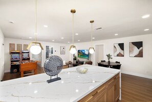 A modern kitchen with a marble countertop, pendant lighting, and a foosball table.