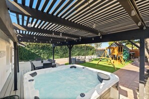 Una vasca idromassaggio sotto una pergola, con un'area giochi sullo sfondo.