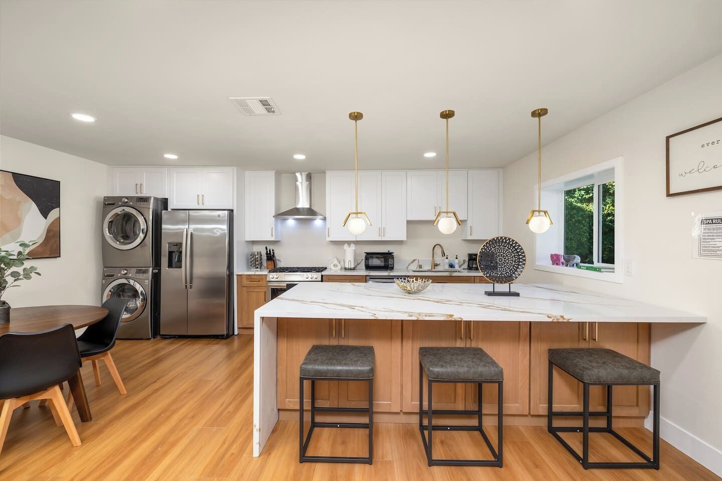 A modern kitchen with stainless steel appliances, a marble island with bar stools, and pendant lighting.