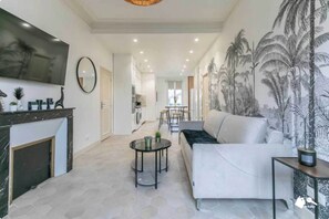 A modern living room with a sofa, a coffee table, and a fireplace. There is a kitchen in the background with a dining area. - 3BDR/8P flat- Villemomble- 20min from Paris by RER (Villemomble)